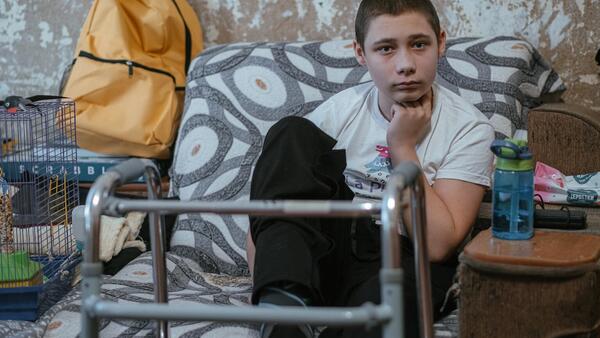 In Nikopol, Kharkiv oblast, eastern Ukraine, Nazar, 13, sits in his family's living room, his walker nearby. His legs and feet were injured by an explosive remnant of war. 