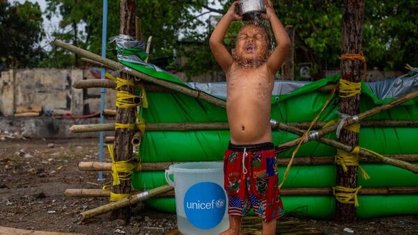 On April 6, 2025, a boy bathes beside a temporary water tank made with tarpaulin provided by UNICEF at a makeshift tent camp in Amarapura township, Mandalay region, Myanmar, following the recent earthquake. 