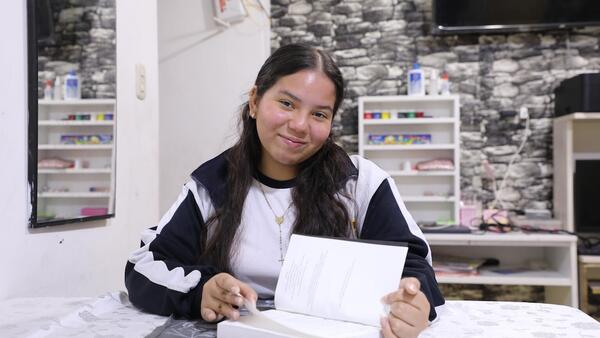 A teenage immigrant from Venezuela reads a book at home in Peru, where she attends school with support from UNICEF and ECW. 