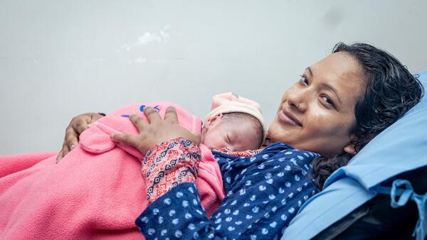 Mother cradles baby in hospital in Nepal where UNICEF supports newborn care.