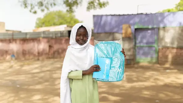 A smiling girl holds her new UNICEF backpack and notebook in Blue Nile State, Sudan.