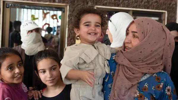 A mother holds a smiling child at a shelter for displaced families in Syria.