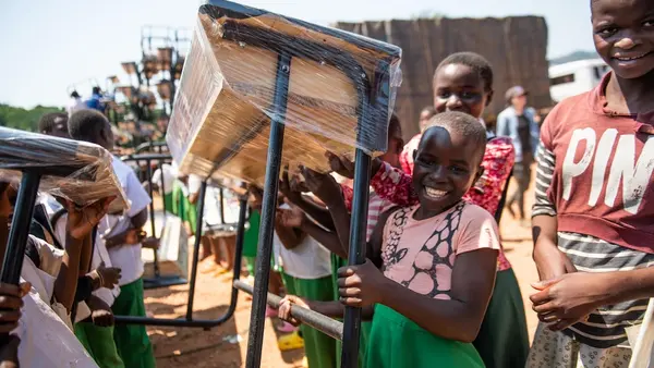 Smiling schoolchildren carry new desks from the K.I.N.D. Fund into Vizara Primary School in northern Malawi in 2024.