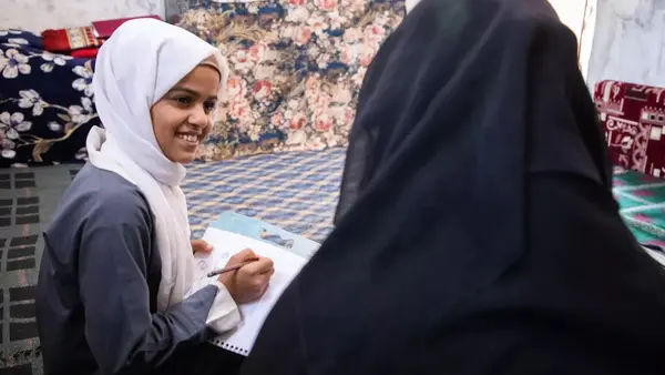 Kholoud, 13, left, talks to her mother while doing homework in the IDP camp where they live in Marib governorate, Yemen.