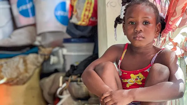 Lovely, 9, sits inside a crowded public space that has served as her family’s shelter since they fled armed group violence in Haiti.