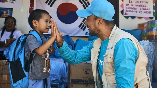 In Bolivia, a young boy who received a UNICEF backpack with school materials high-fives a UNICEF staff person.