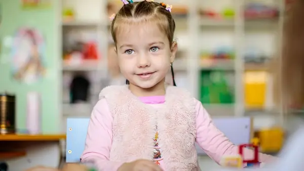 A little girl in a fluffy vest sits at a desk during a preschool development class organized by UNICEF at a library in Bortnyky, Lvivska region, Ukraine.