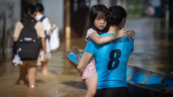 In Vietnam, mother carries her youngest daughter through flooded streets following consecutive typhoons.