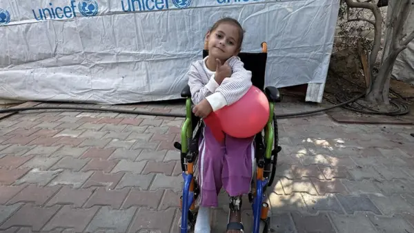 A girl in a wheelchair holds a balloon outside a UNICEF tent in central Gaza. 