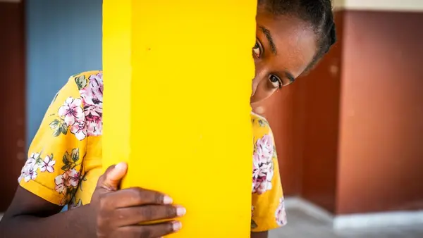 A young girl in Gabon peeks out from behind a pillar inside a child protection service center supported by UNICEF. 