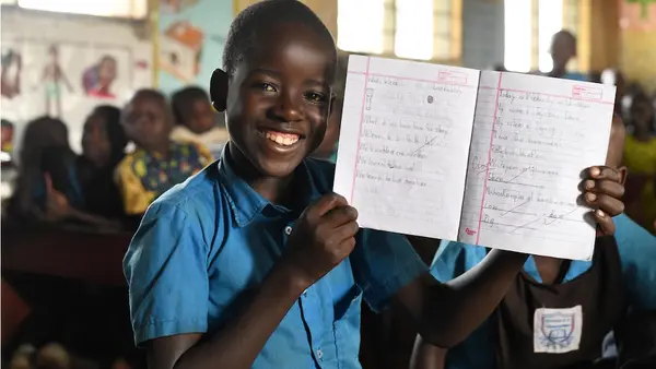 Edison, 11, a UNICEF-supported primary school student in Uganda, smiles while showing work he completed in his school notebook. 
