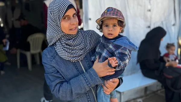 A mother holds her 1-year-old son outside a UNICEF-supported nutrition point in southern Gaza.