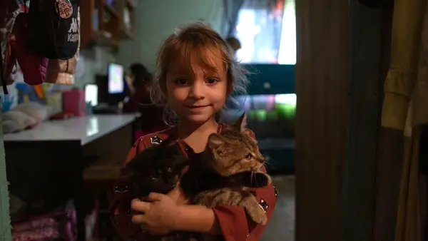 A little girl holds a cat in the dimly lit house in Staryi Saltiv, Kharkiv region, Ukraine. 