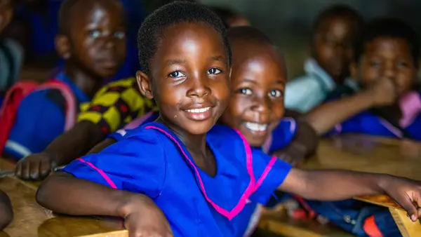 Two girls smile at their school in Malawi, where UNICEF is working to expand access to education