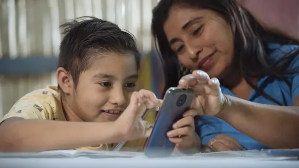 A mother in Ecuador helps her 9-year-old son with his homework using his cell phone.