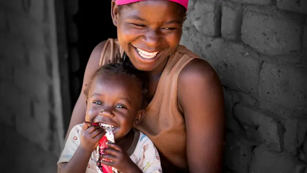 20-year-old Edna Maunde smiles as her daughter, 2 year 4 months old Christina Cosmas eats RUTF at their home in Mavila Village, Zomba, southern Malawi on Thursday, 8 June 2023.
