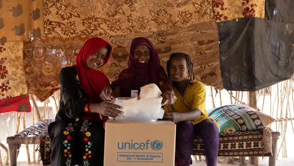 A mother and her daughters open a box containing UNICEF dignity kits in Aldamer, River Nile State, Sudan.