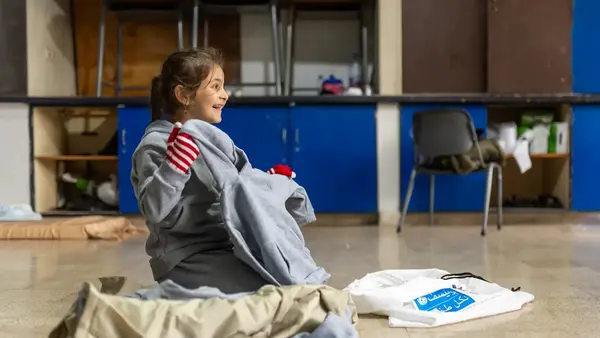 A girl displaced by violence in Lebanon opens a UNICEF winter clothing kit. 