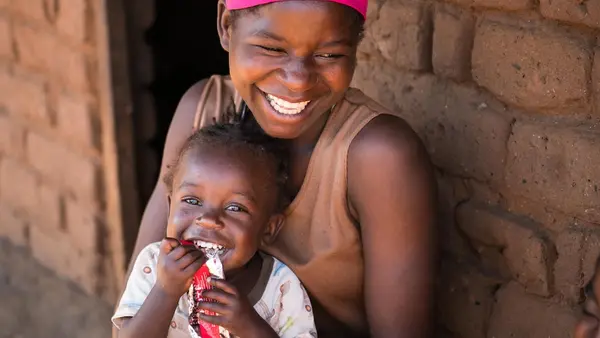 Edna Maunde, 20, smiles as her daughter, 2-year-old Christina, eats RUTF at their home in Mavila Village, Zomba, southern Malawi, on June 8, 2023.