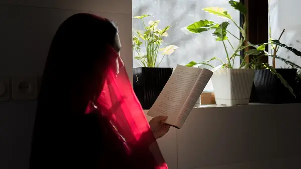 An 18-year-old girl in Afghanistan sits at home reading a book.