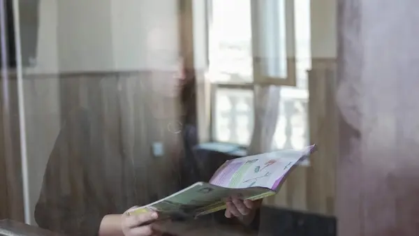 A In Afghanistan on July 23, 2026, a 14-year-old girl stands by a window in her house, reading a book. 