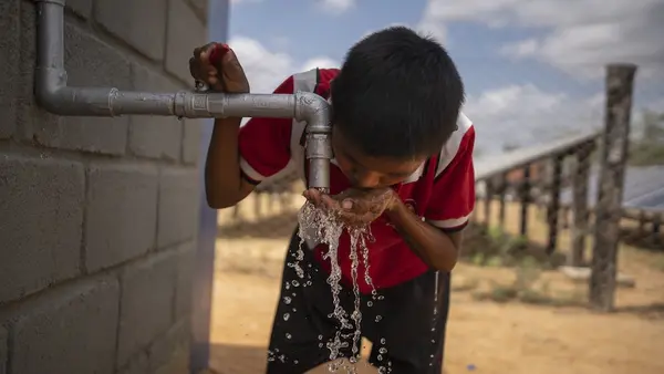 Young boy cups hands, drinking from spigot of clear water