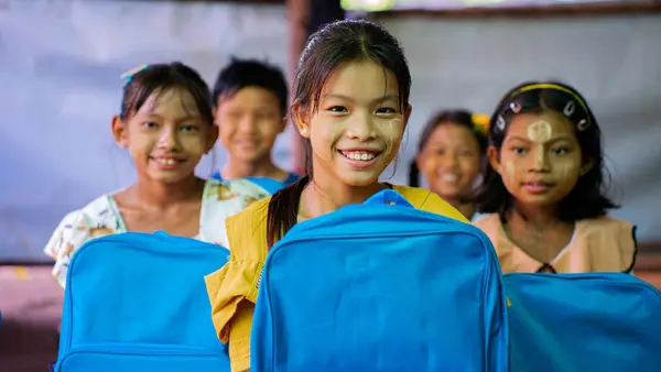 A group of girls in Myanmar proudly hold backpacks supplied by UNICEF. 