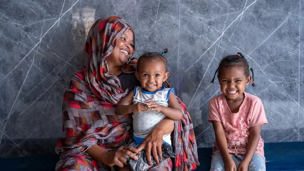 Woman holding small child, seated next to young girl, all smiling