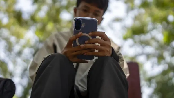 A young person scrolls through social media alone on a city street.