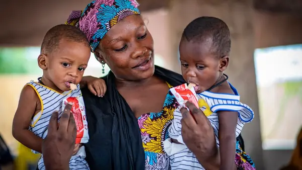 Women holding her two children while they eat RUTF
