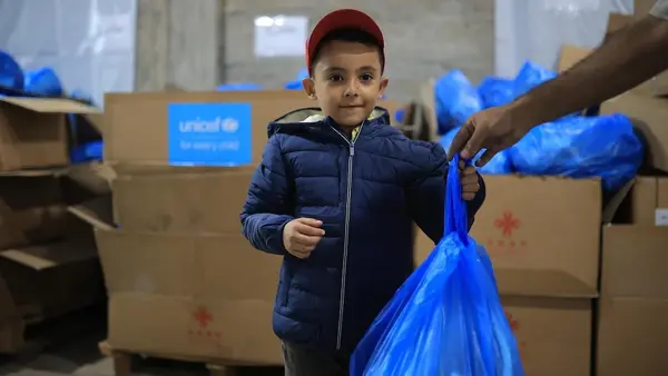 On Oct. 6, 2026 in Gaza, a child wears a warm jacket he received from UNICEF as a staff member hands him a bag of winter clothing.