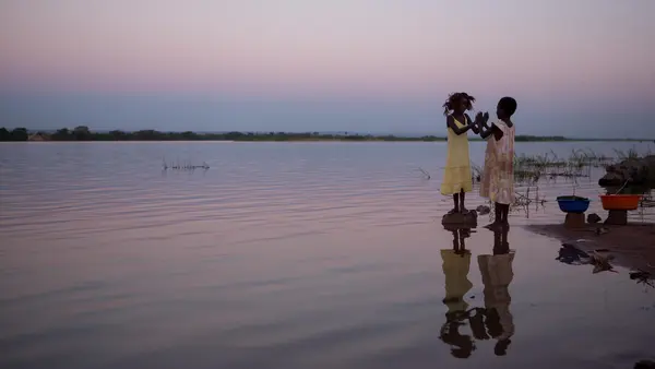 Two young girls play happily on the banks of the Luapala river at sunset in the Democratic Republic of the Congo. 