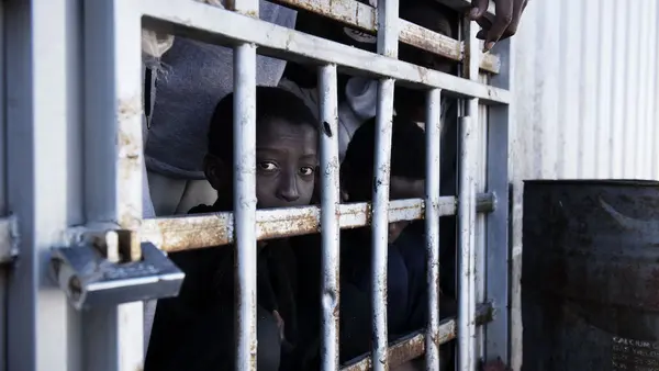 Child migrant looking through the bars of a detention cell in Libya.