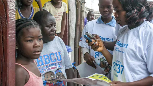 adolescent girls, holding brochures, read text messages on mobile telephones in the West Point neighbourhood of Monrovia, the capital. The girls, who are ‘U-Reporters’ are helping to raise awareness in the community about Ebola virus disease