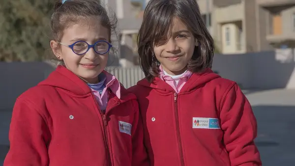 Arah (right) and Saba (left), Syrian refugees living in the Kurdistan Region of Iraq, wear their new winter uniforms at Rubar School in Erbil. 