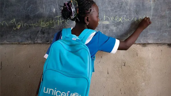 Girl with a UNICEF Backpack Writing on Blackboard