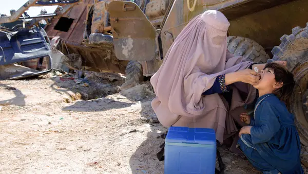 UNICEF-supported polio worker Afia (name changed), 19, vaccinates a child in an old military barrack in Afghanistan in March 2018. 