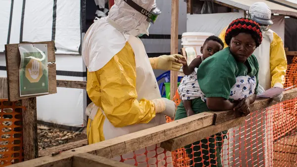 A health worker wearing a gown, gloves and goggles checks a child potentially infected with Ebola being carried on the back of a caregiver at the Ebola Treatment Center of Beni, North Kivu province, Democratic Republic of Congo on March 24, 2019.