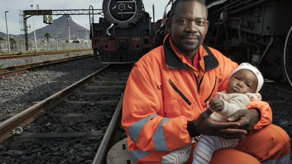 In May 2019, Congolese refugee Dieu-Merci Matala, 44, holds his infant daughter, Grace, near the Transnet harbor facility where he works in Cape Town, South Africa. 