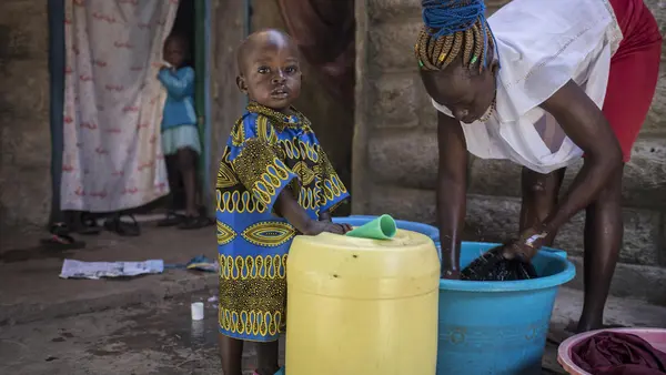 On 3 October 2020 in Kenya, Cinderella Akinyi Othiambo, 22, washes clothes as her one-and-a-half-year-old nephew, Duncan Makoa, looks to the camera, outside her home in Mathare, an informal settlement in Nairobi.