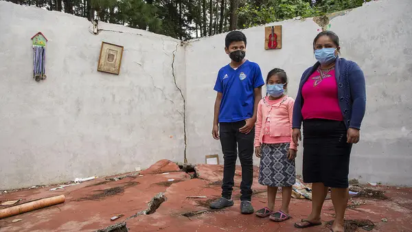 A mother with her two children stand in what remains of their home in Guatemala after storms Eta and Iota swept through, forcing them to flee to a temporary shelter.