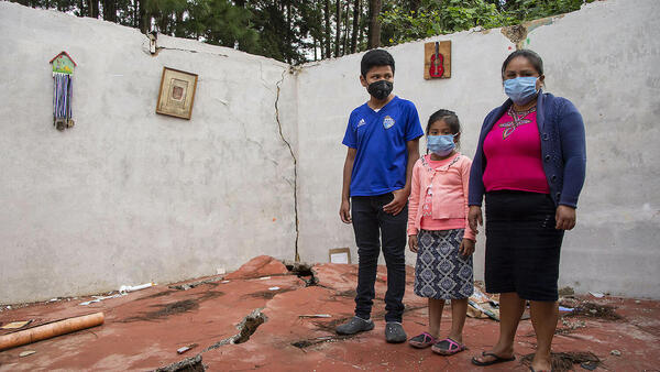 A mother with her two children stand in what remains of their home in Guatemala after storms Eta and Iota swept through, forcing them to flee to a temporary shelter.