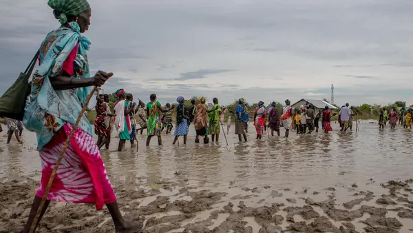 Displaced families make their way back to temporary housing through flood water after a distribution point ran out of supplies in Pibor, Boma State, South Sudan on November 6, 2019. 