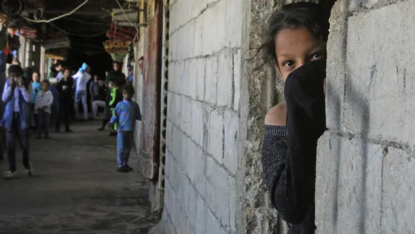 On March 17, 2020, a Syrian refugee, her face covered to protect against COVID-19, looks out from a doorway in an unfinished building where she has been living in the city of Sidon in southern Lebanon. 