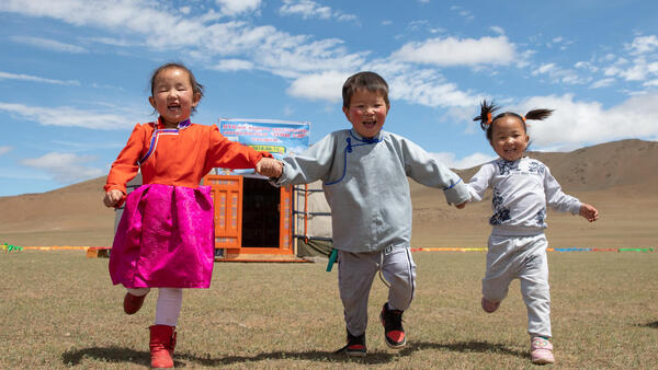 On June 17, 2018, in Mongolia, three laughing children run hand-in-hand outside the newly opened mobile ‘ger’ (traditional nomadic tent) kindergarten.