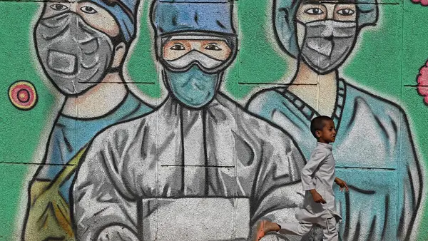 On March 21, 2021 in India, a child runs past a mural depicting frontline health care workers, along a road in New Delhi.