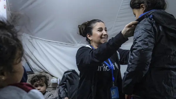 A UNICEF staffer helps a child try on a winter coat from a new winter clothing kit distributed by UNICEF and partners to families living in Roj IDP camp, northeastern Syria. 
