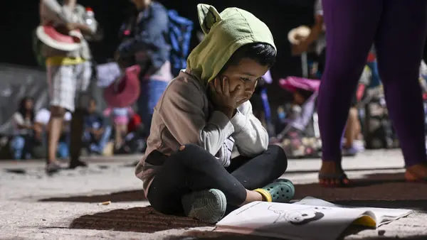 A child migrant sits on the floor with a coloring book.