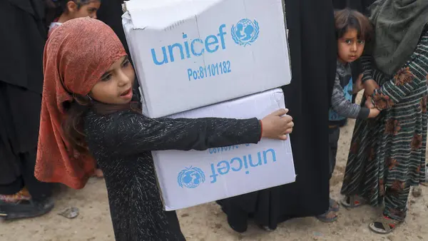 Displaced Syrian children help their parents distribute winter clothes from UNICEF at the Al-Hol camp in Hasakah, northeast Syria, on March 2, 2022.