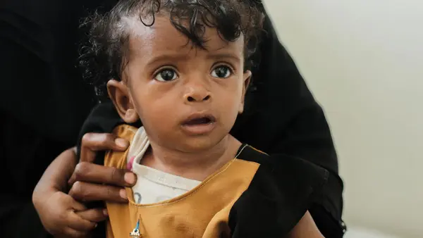 A child waits with her caregiver to receive treatment for severe acute malnutrition